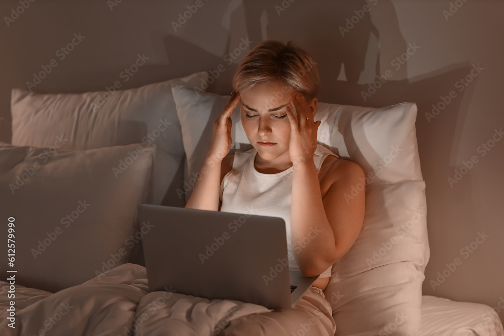 Sleepy young woman using laptop in bed at night