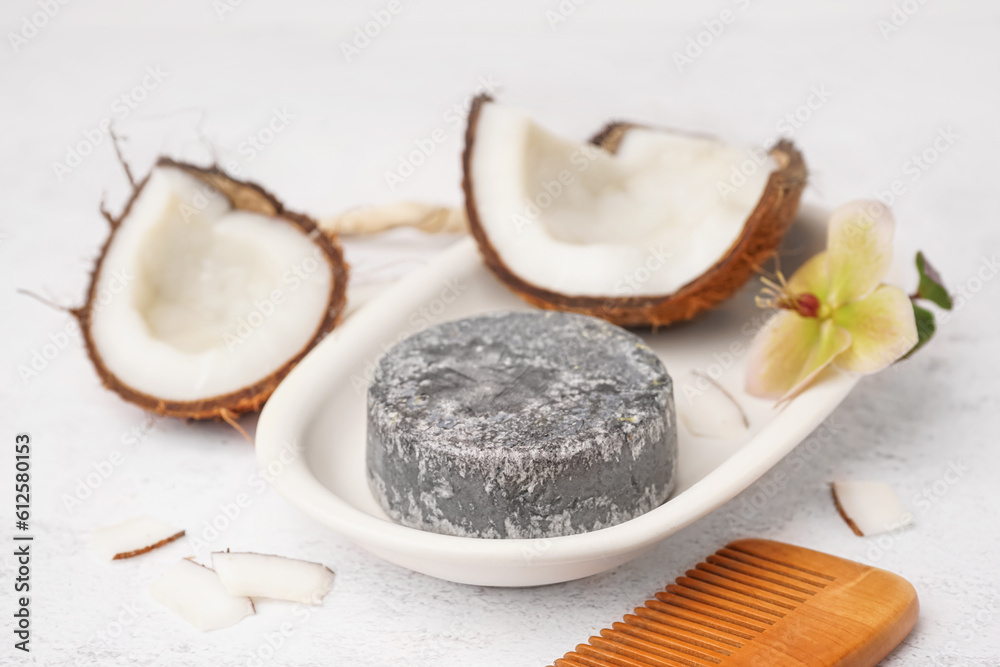 Stand with handmade solid shampoo, coconut, orchid flower and hair comb on light background, closeup