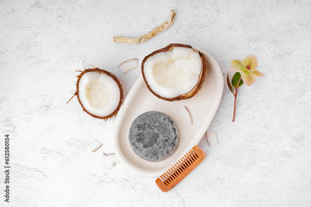 Stand with handmade solid shampoo, coconut, orchid flower and hair comb on light background