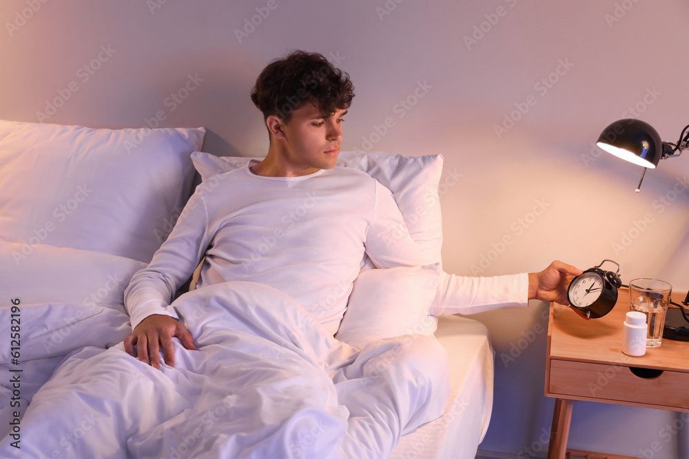 Young man watching time in bed at night