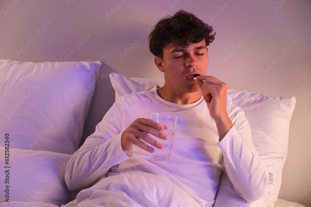 Young man taking pill before sleep in bed at night