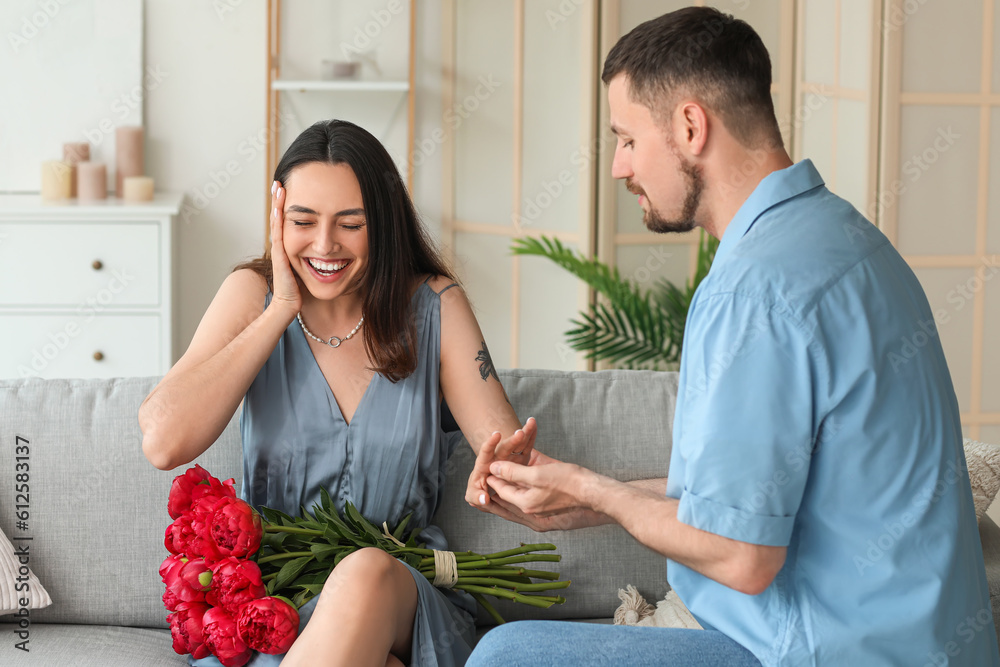 Young man putting engagement ring on his girlfriends finger at home