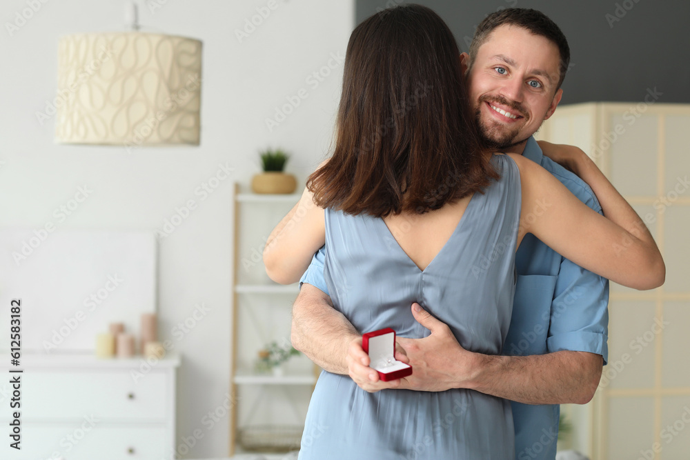 Young man with engagement ring hugging his girlfriend at home