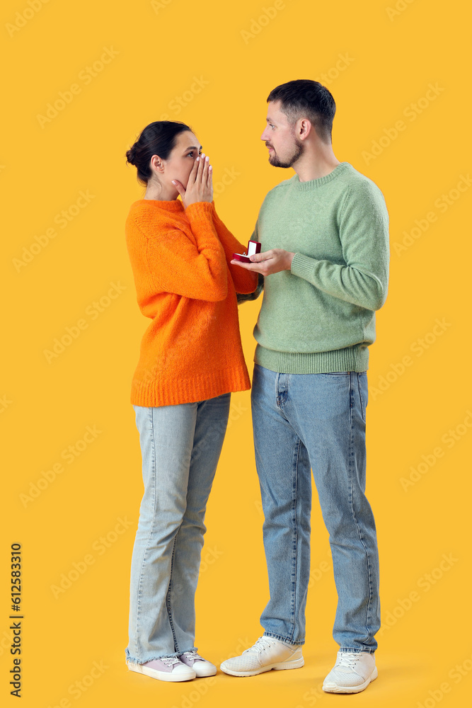 Young man proposing to his girlfriend on yellow background