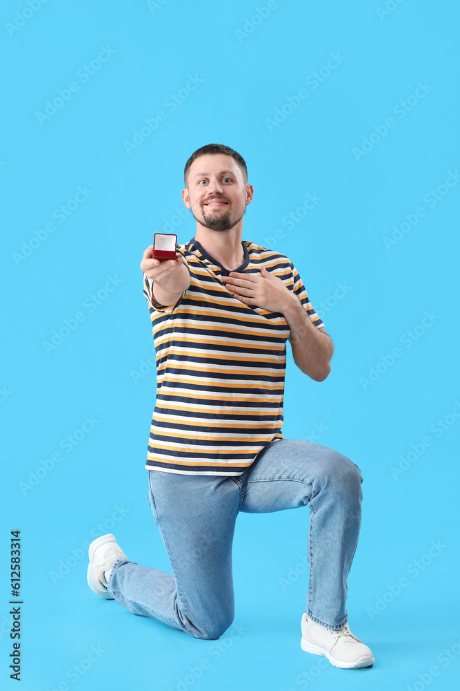 Handsome man with engagement ring on blue background