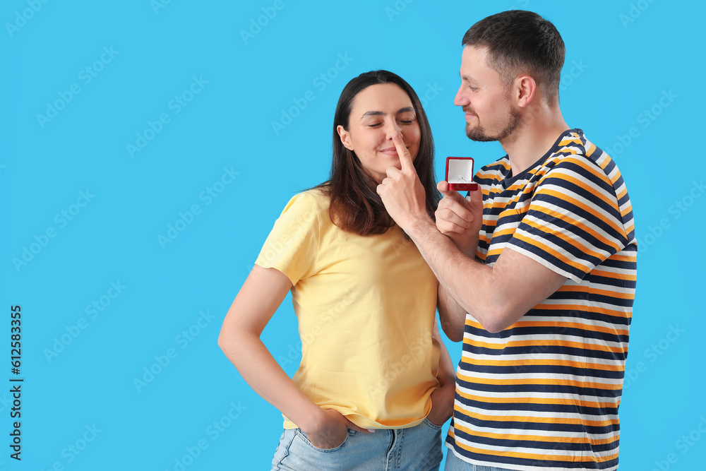 Happy young couple with engagement ring on blue background