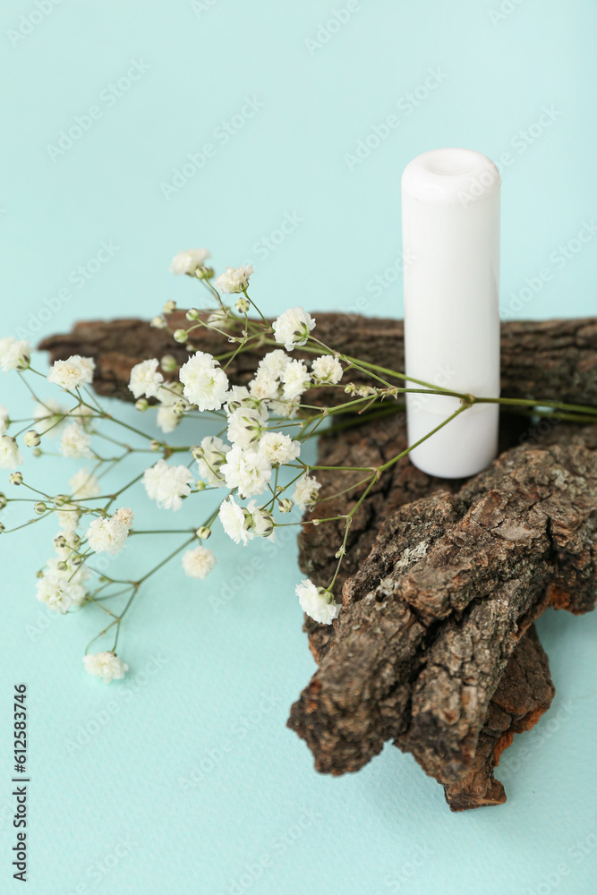 Lip balm, tree bark and gypsophila flowers on color background, closeup