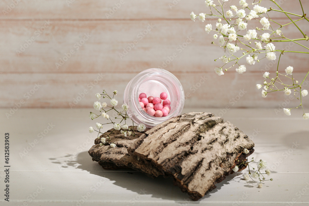 Jar of blush balls, tree bark and gypsophila flowers on light wooden table