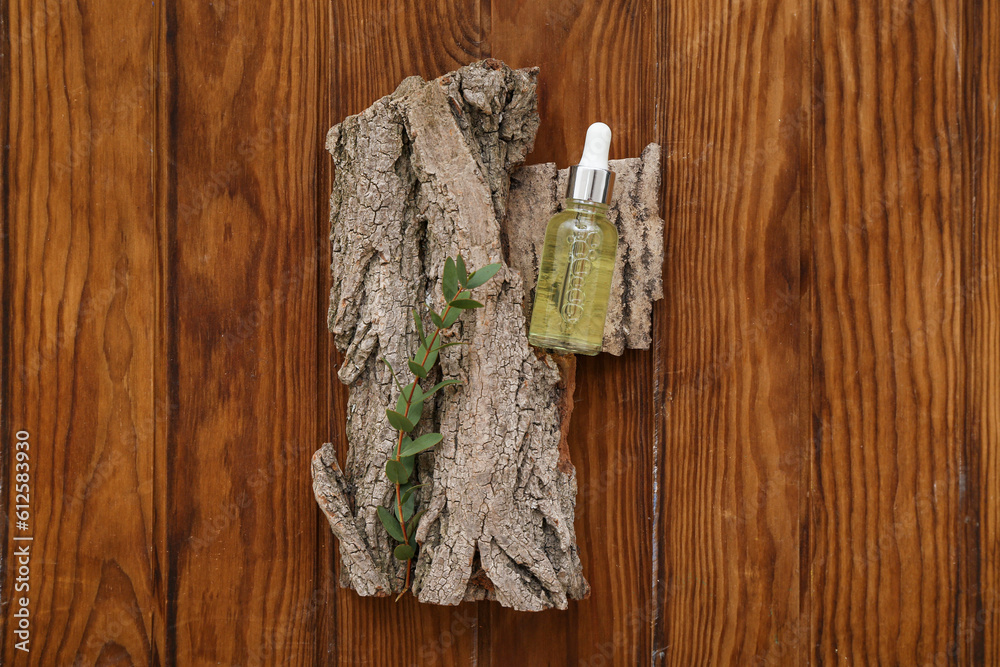 Bottle of essential oil, tree bark and eucalyptus branch on wooden background