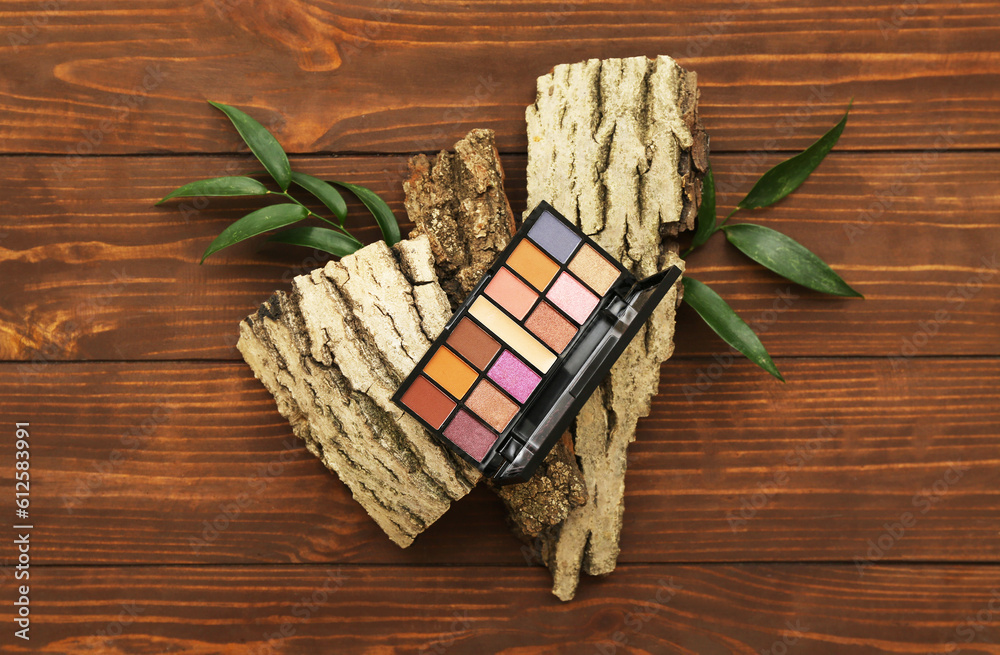 Palette of eyeshadows, tree bark and plant leaves on wooden background