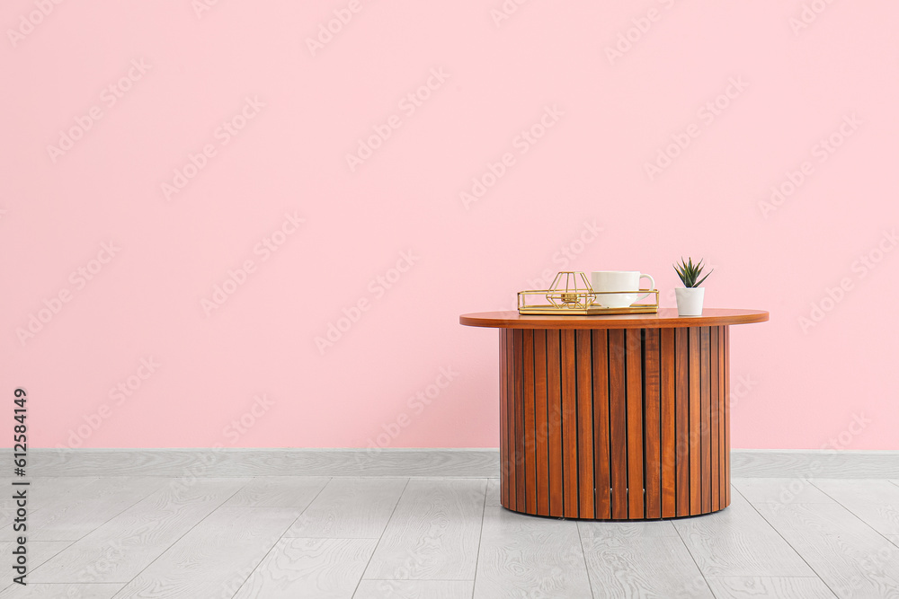 Wooden coffee table with houseplant, tray and cup near pink wall