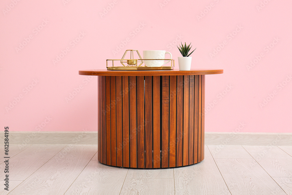 Wooden coffee table with houseplant, tray and cup near pink wall