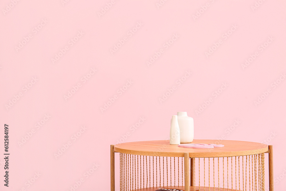 Wooden coffee table with vases near pink wall