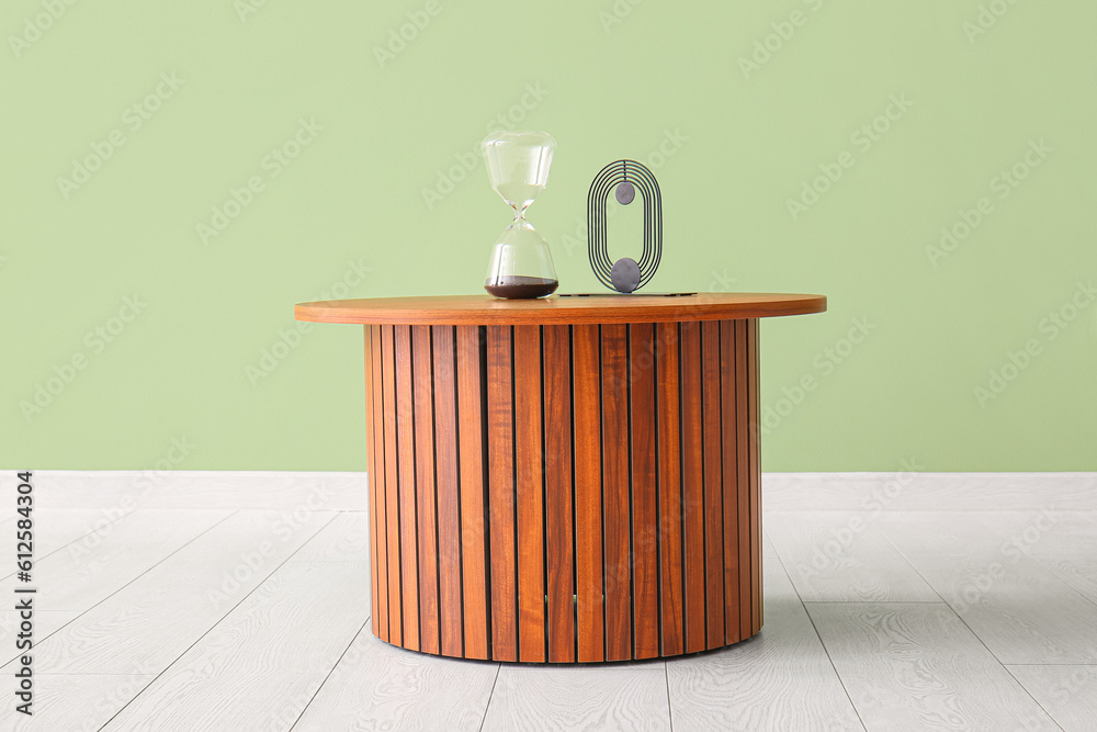 Wooden coffee table with hourglass and decorative figure near green wall