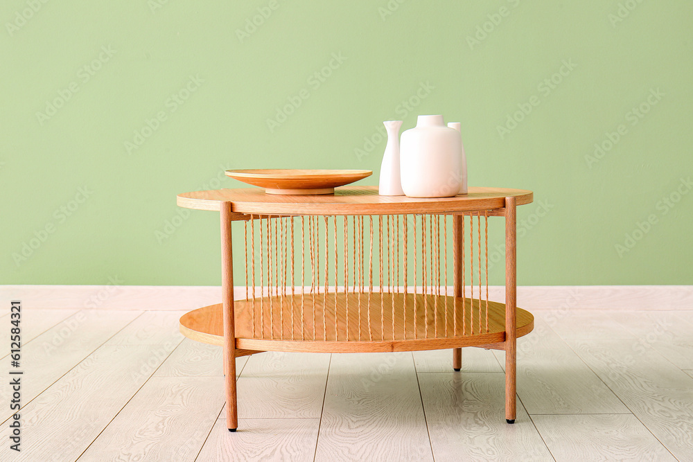 Wooden coffee table with wooden plate and vases near green wall