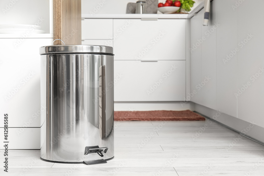 Metallic trash bin near table in interior of modern kitchen