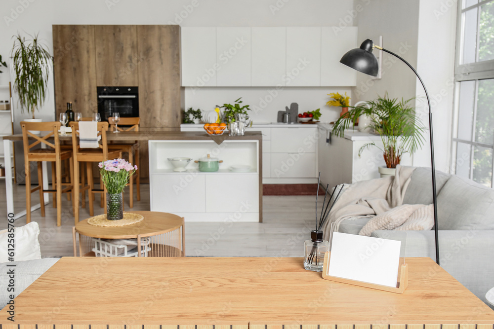 Blank photo frame and reed diffusers on wooden table in interior of open plan kitchen