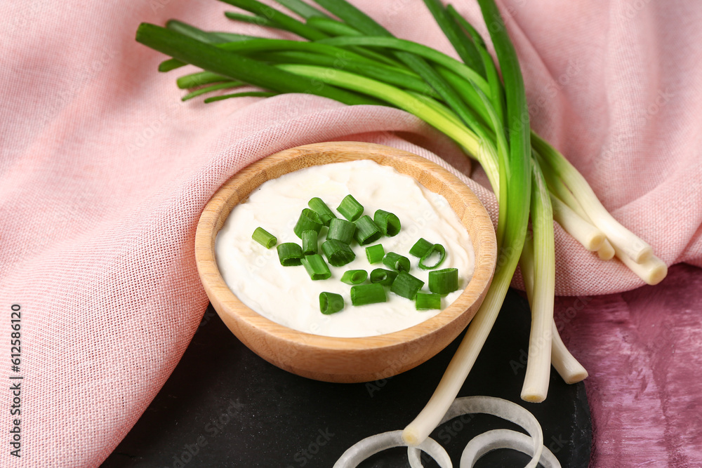 Bowl of tasty sour cream with sliced scallion and onion on pink background