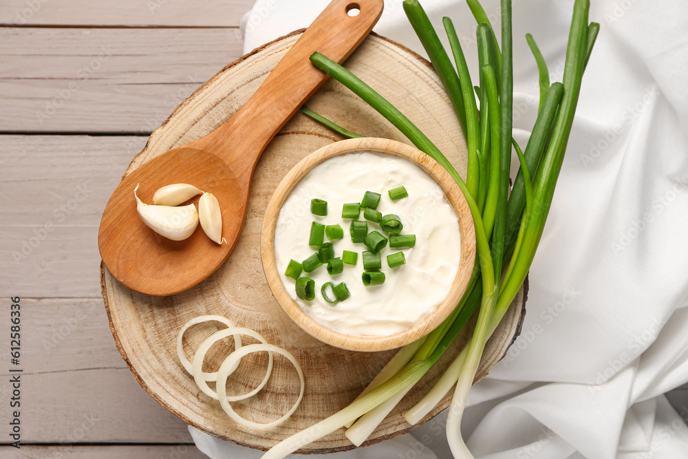 Bowl of tasty sour cream with sliced scallion and onion on grey wooden background