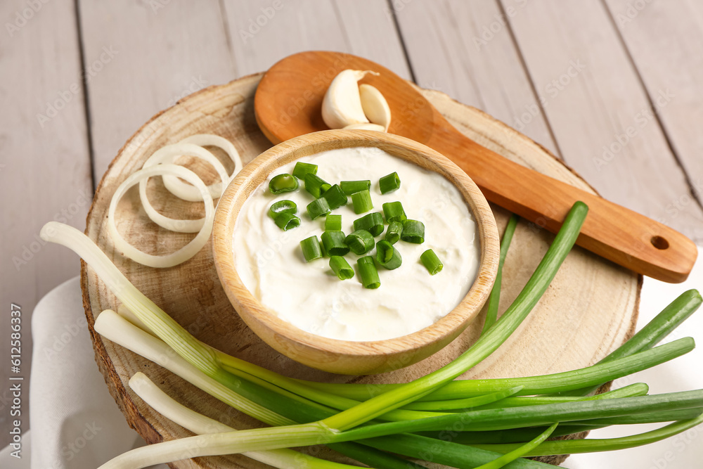 Bowl of tasty sour cream with sliced scallion and onion on grey wooden background