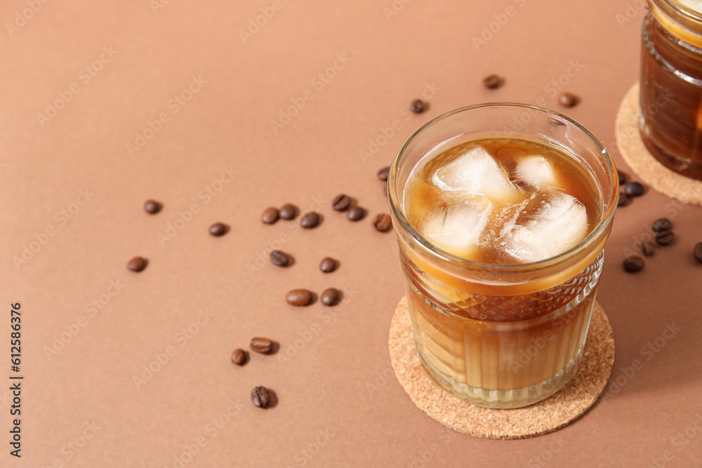 Glasses of ice coffee with beans on beige background