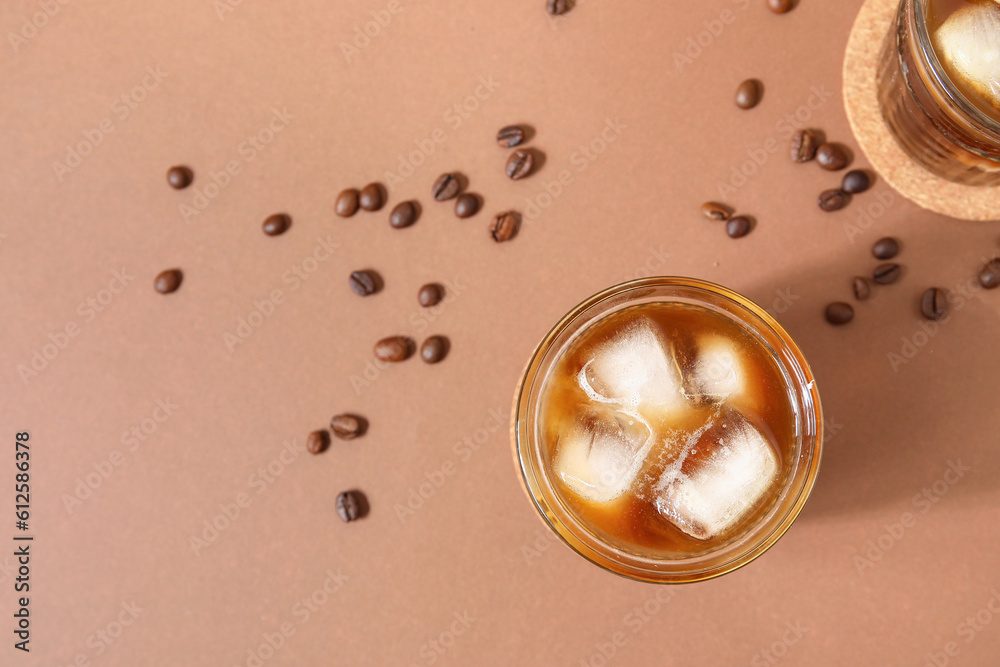 Glasses of ice coffee with beans on beige background