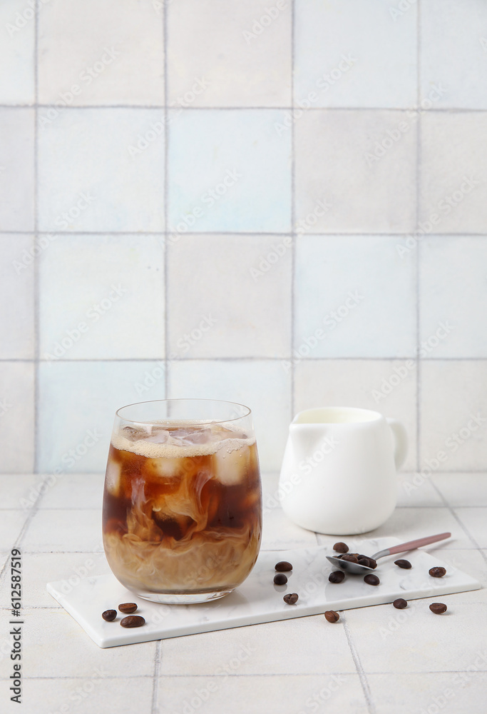 Glass of tasty ice coffee with milk on white tile background