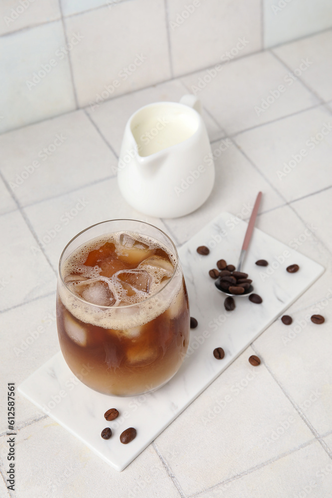 Glass of tasty ice coffee with milk on white tile background