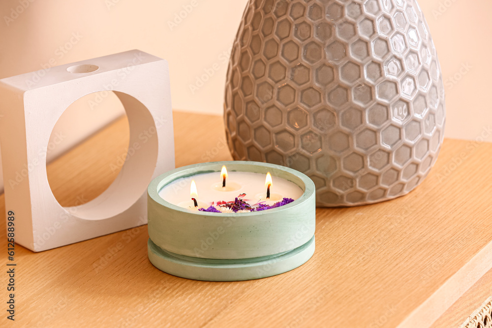 Holder with burning candle and decor on table near beige wall in room, closeup