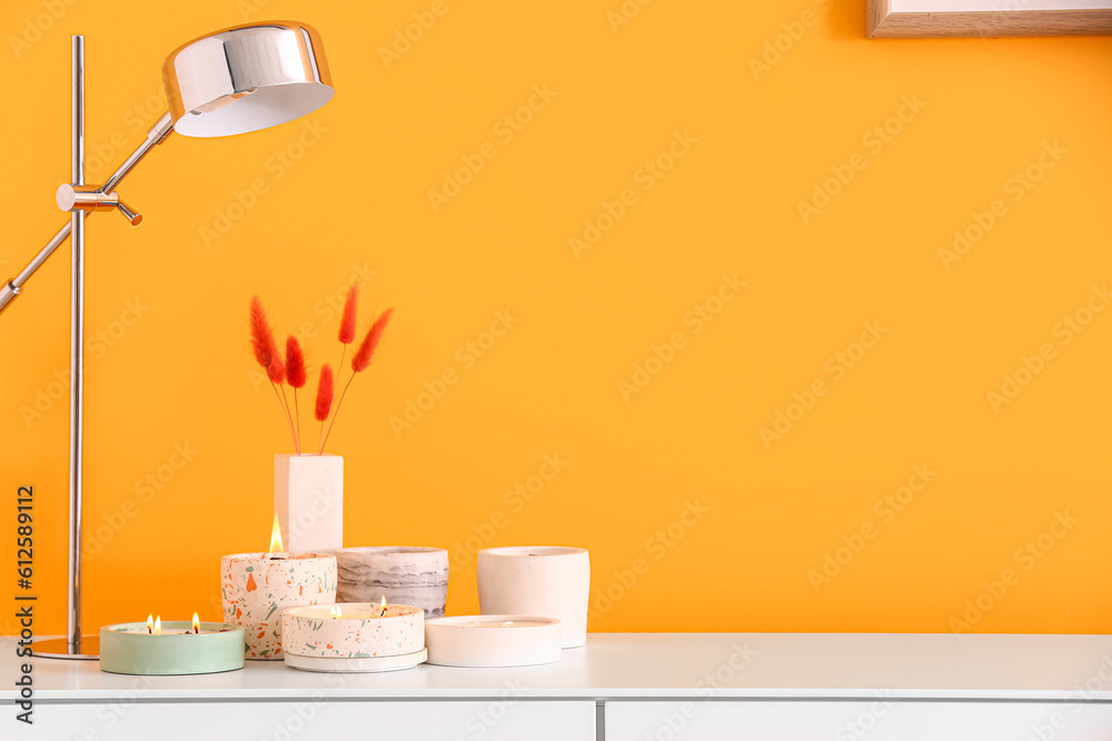 Holders with burning candles and lamp on table near orange wall in room