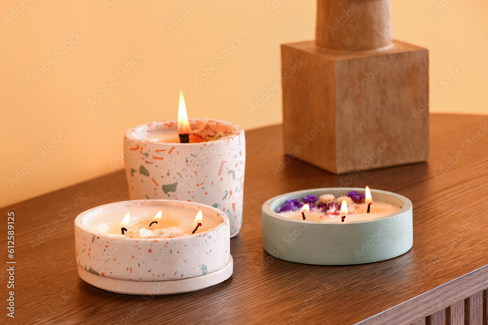 Holders with burning candles on wooden table near orange wall in room