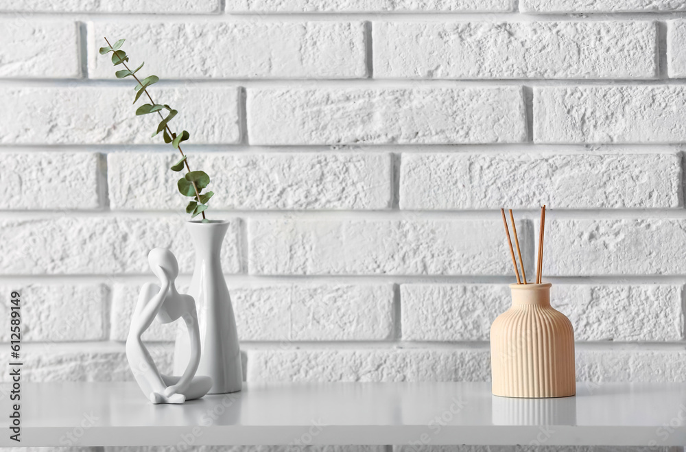 Bottle of reed diffuser and eucalyptus branch on table near light brick wall in room