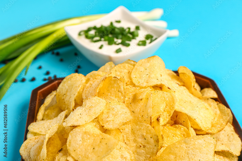 Bowl of tasty sour cream with sliced green onion and potato chips on blue background