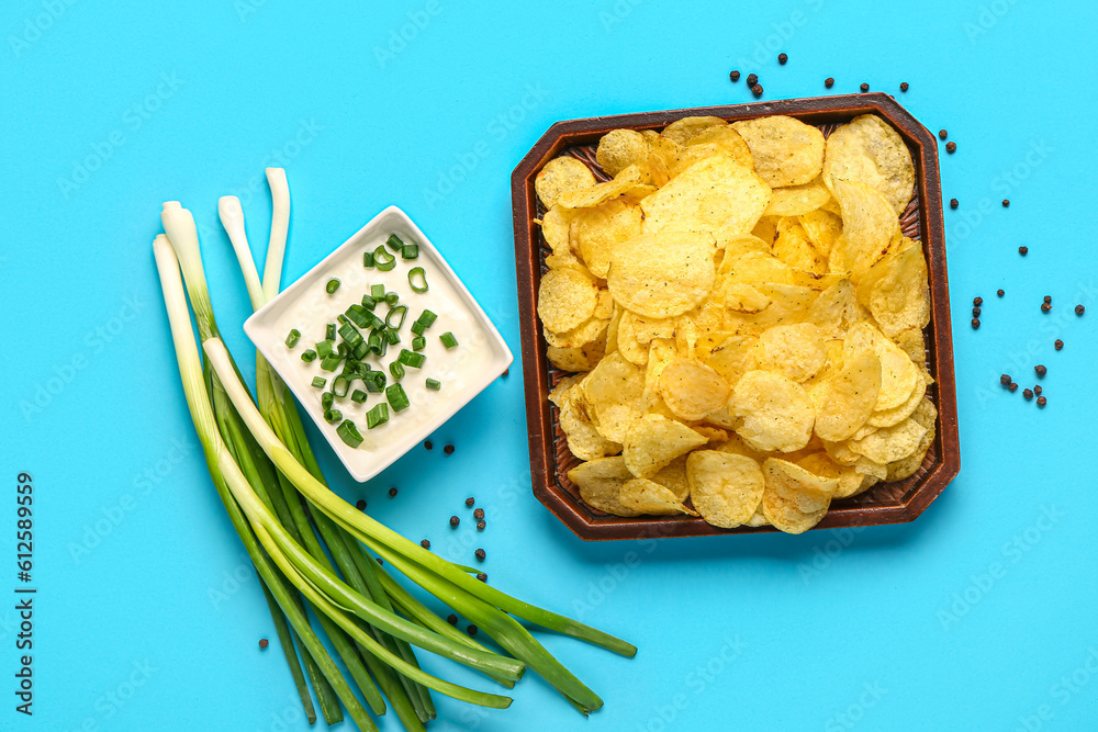 Bowl of tasty sour cream with sliced green onion and potato chips on blue background