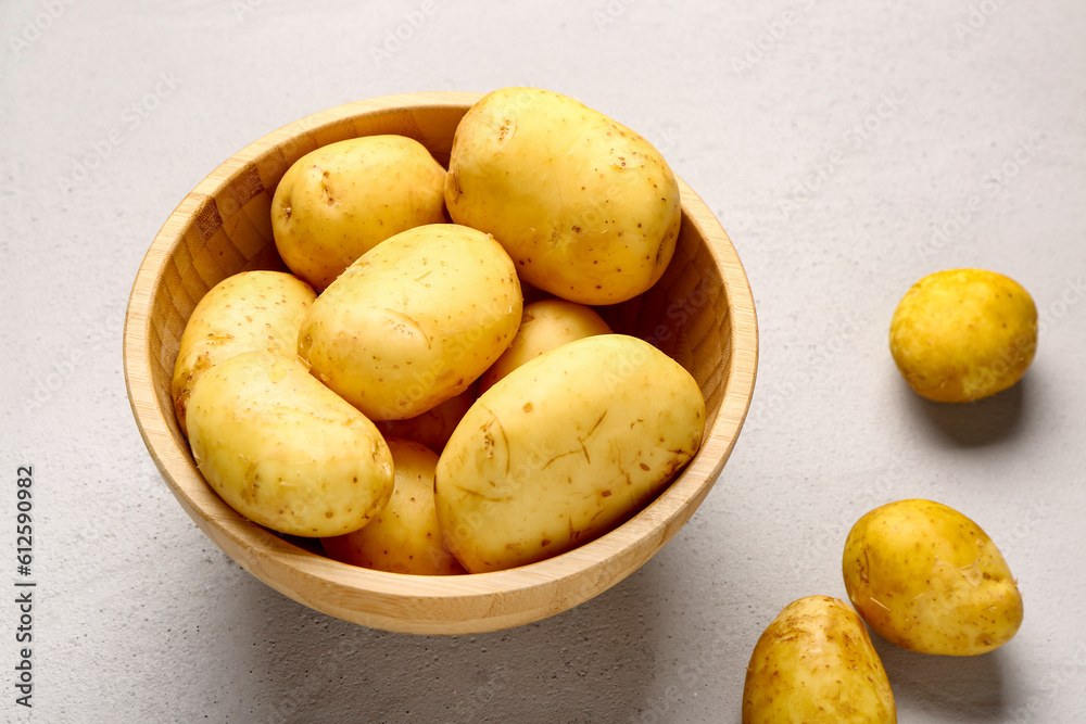 Wooden bowl with raw baby potatoes on grey background