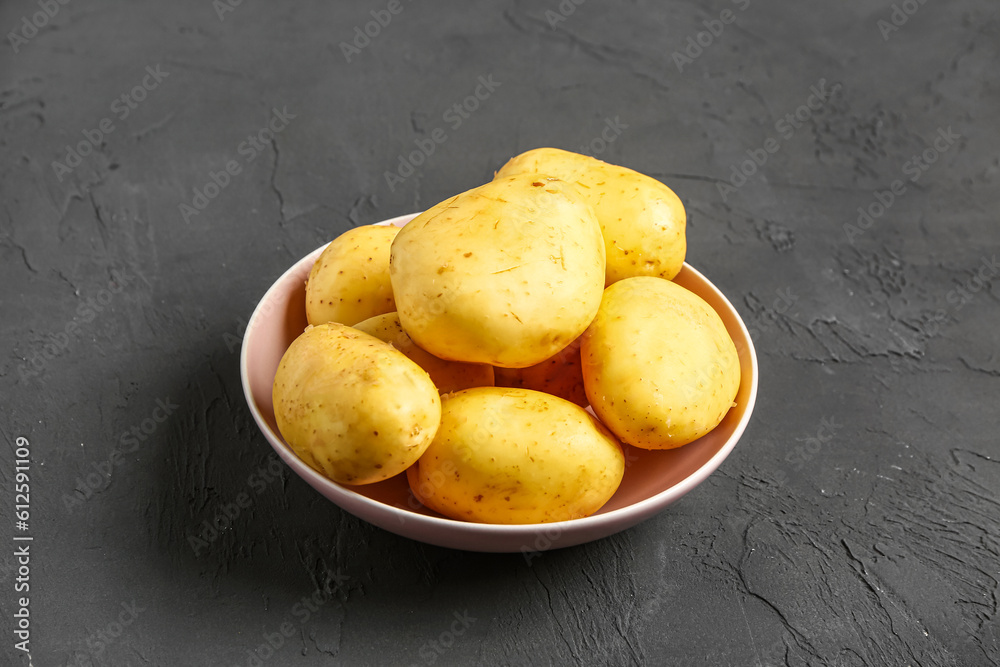 Bowl with raw baby potatoes on black background