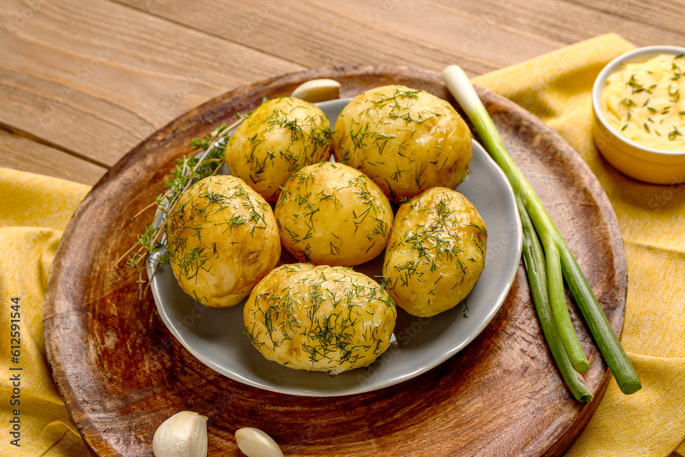 Plate of boiled baby potatoes with dill and green onion on wooden background