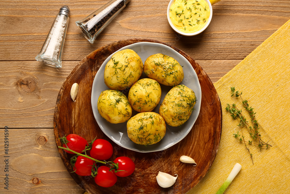 Plate of boiled baby potatoes with dill and tomatoes on wooden background