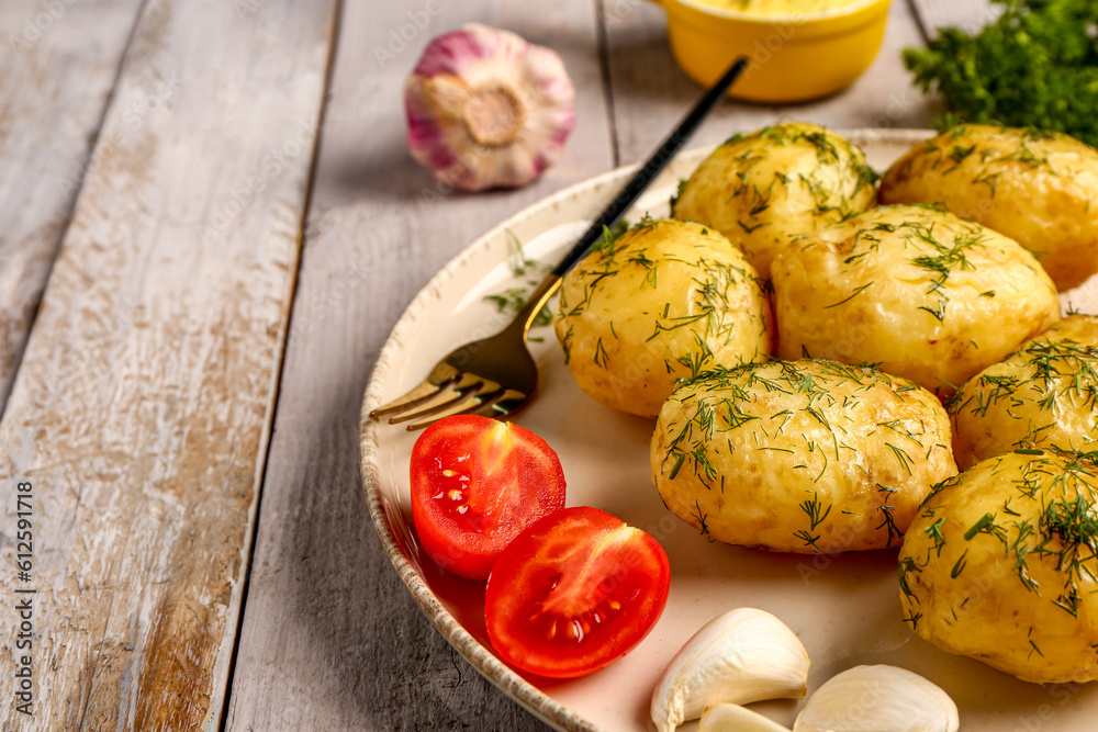 Plate of boiled baby potatoes with dill and tomatoes on grey wooden background