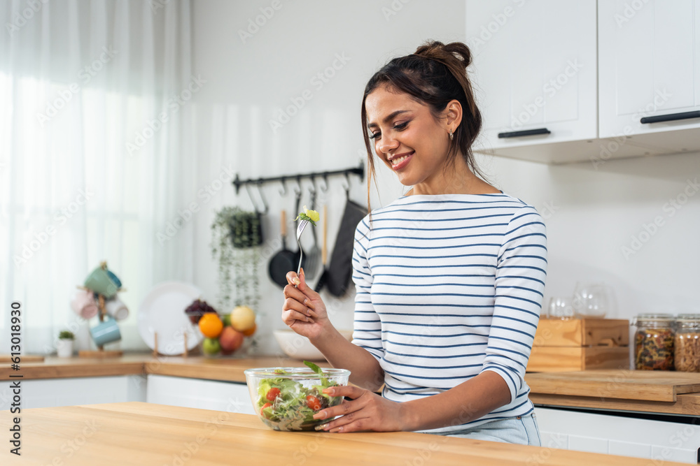 Caucasian young woman eating healthy green salad in kitchen at home. 