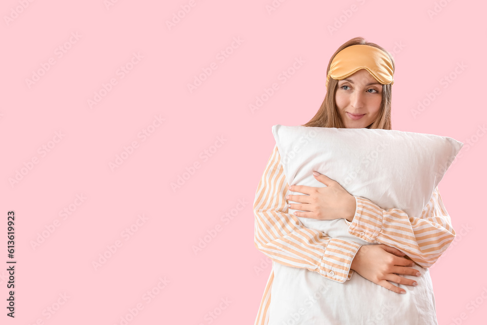 Young woman with sleeping mask and soft pillow on pink background