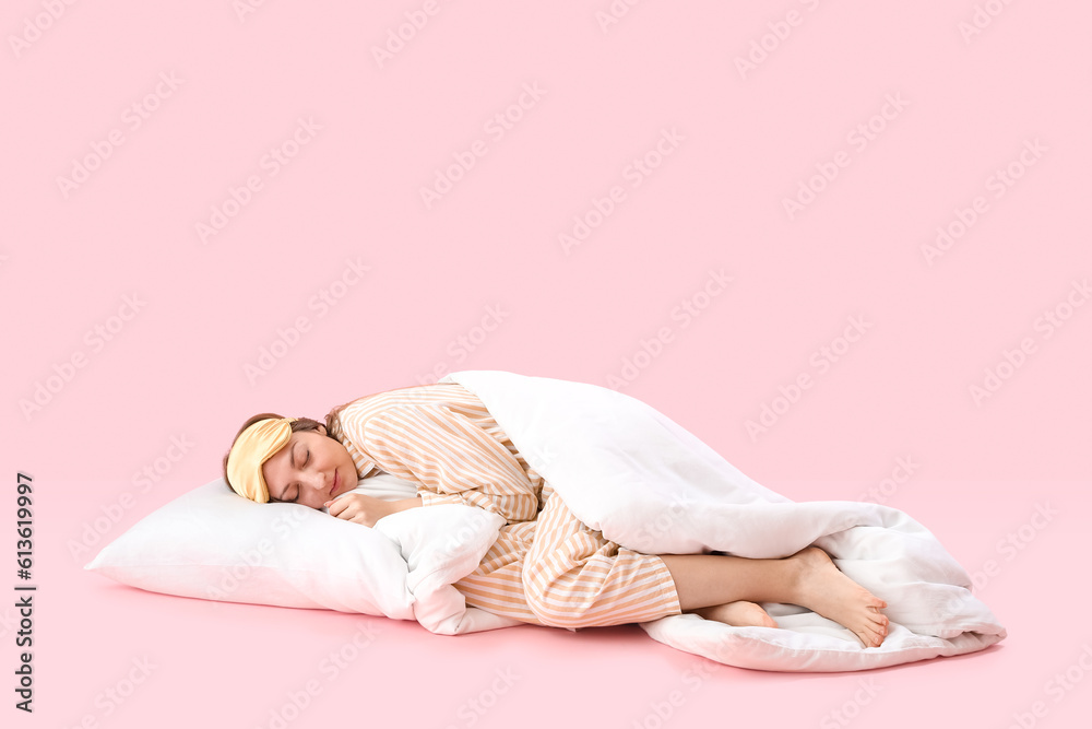 Young woman in pajamas with blanket and pillow sleeping on pink background