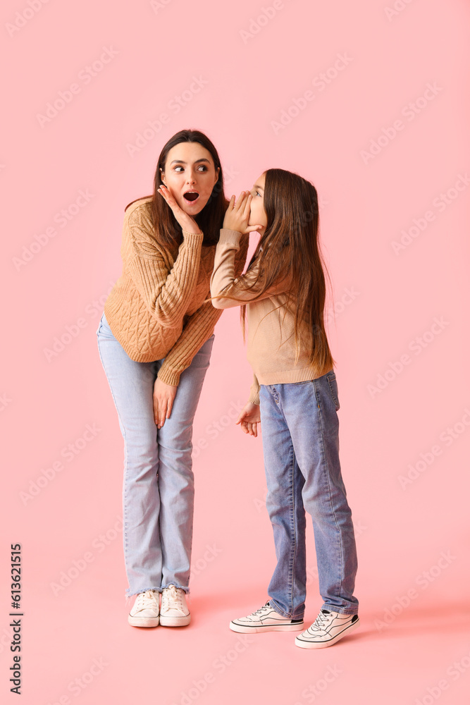 Little girl telling secret to her shocked mother on pink background