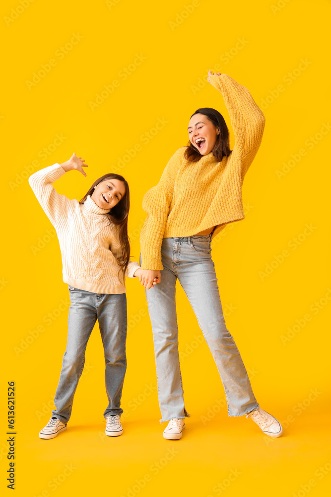 Little girl and her mother in knitted sweaters dancing on yellow background