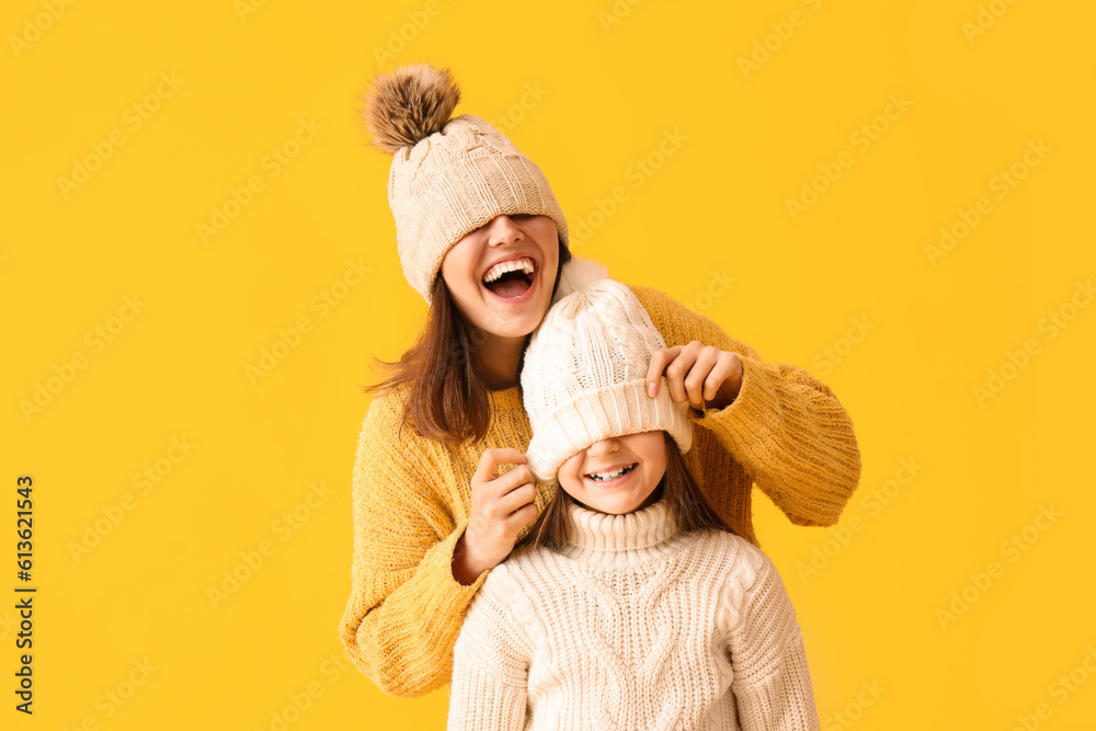 Little girl and her mother in warm hats and sweaters on yellow background