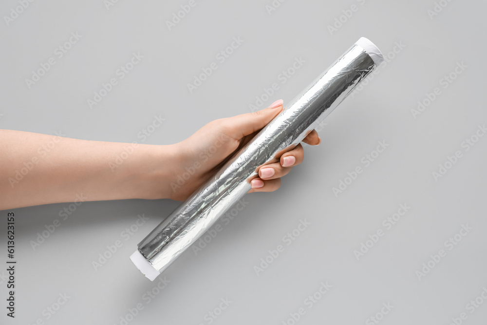 Female hand with aluminium foil roll on grey background