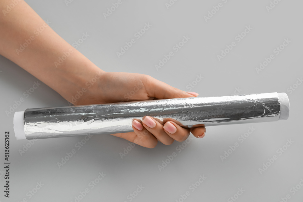 Female hand with aluminium foil roll on grey background, closeup