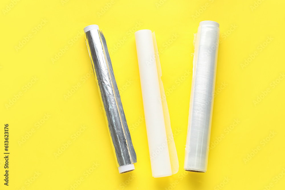 Rolls of aluminium foil, food film and baking paper on yellow background