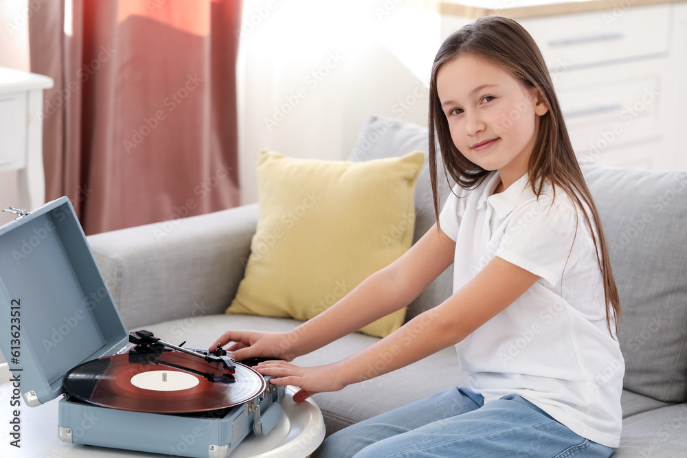 Little girl with record player sitting on sofa at home