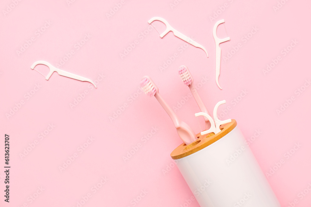 Overturned toothbrush holder and floss toothpicks on pink background